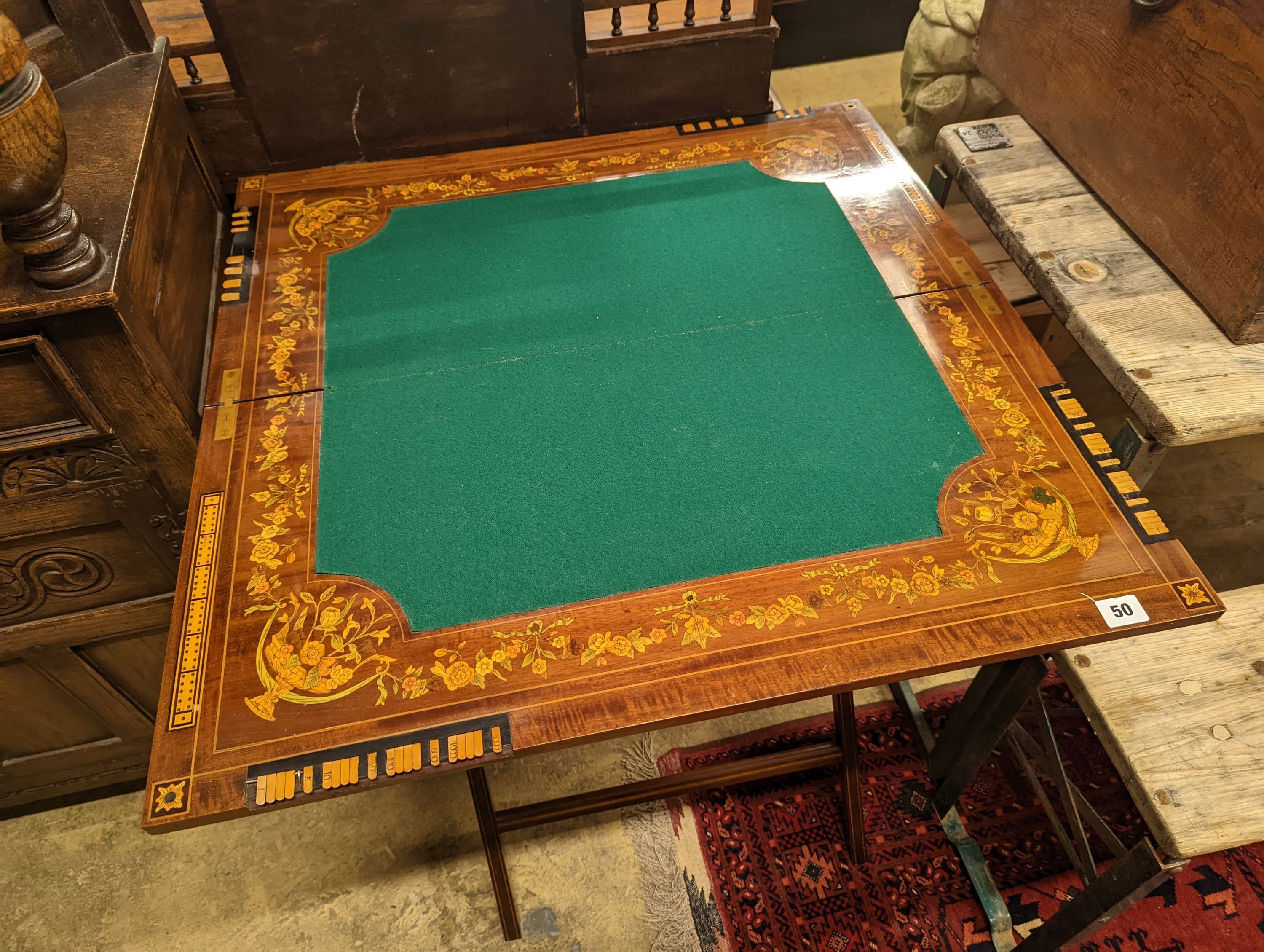 An Edwardian marquetry inlaid mahogany folding games table by W. Thornhill & Co., London, the interior baize lined surface with cribbage board and hinged markers, width 76cm, height 76cm